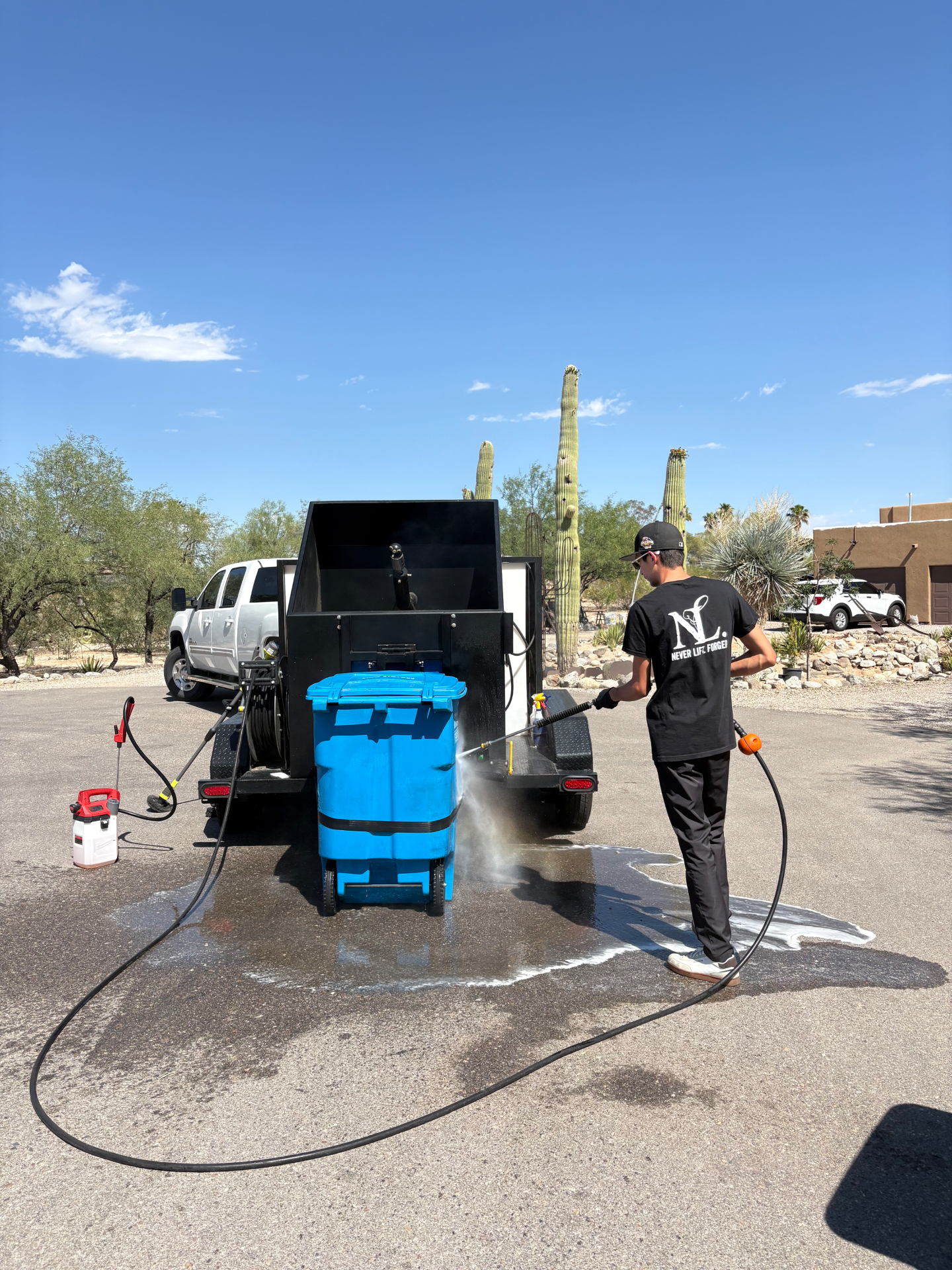 The Trash Talkers technician power washing a blue trash bin at a Tucson home